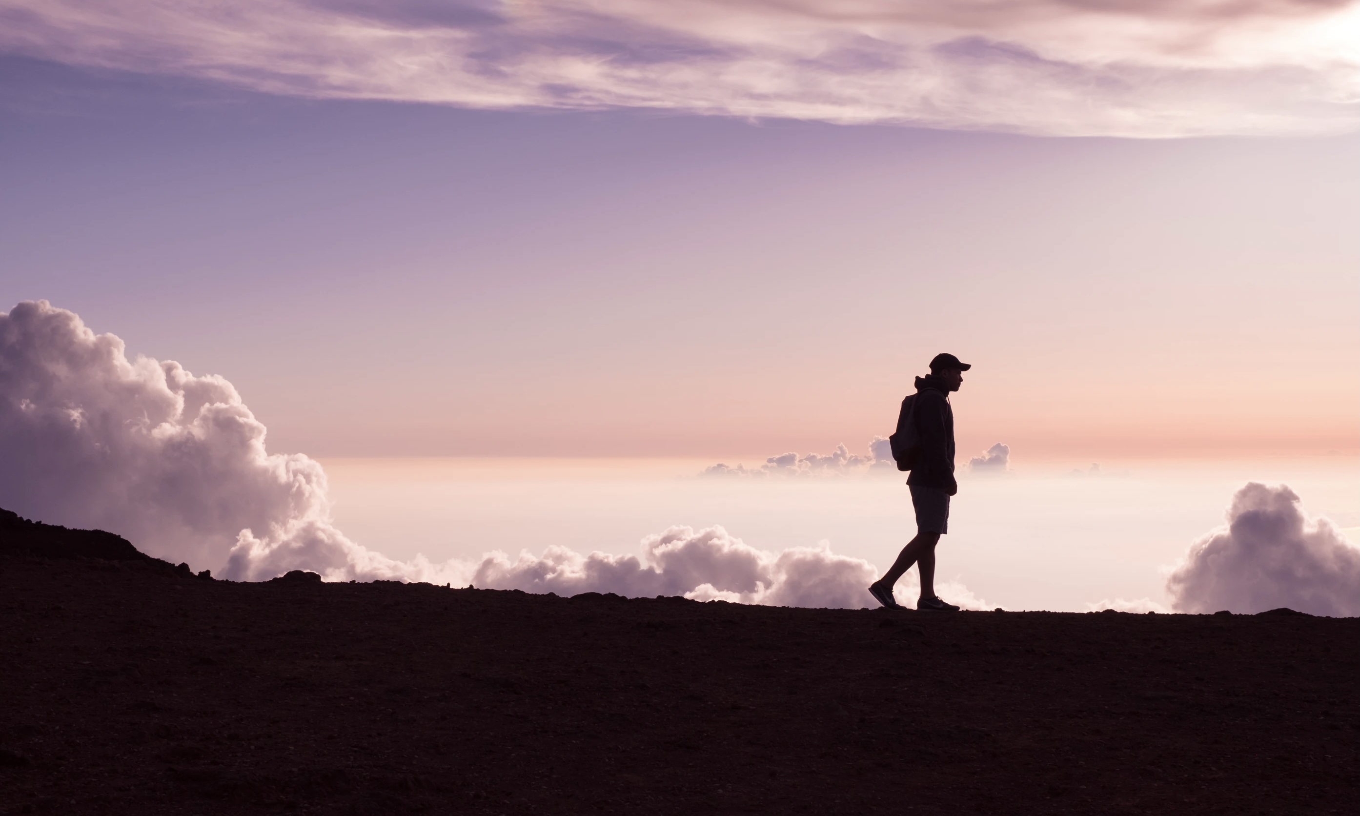 Silhouette of Man Walking in Front of Clouds
